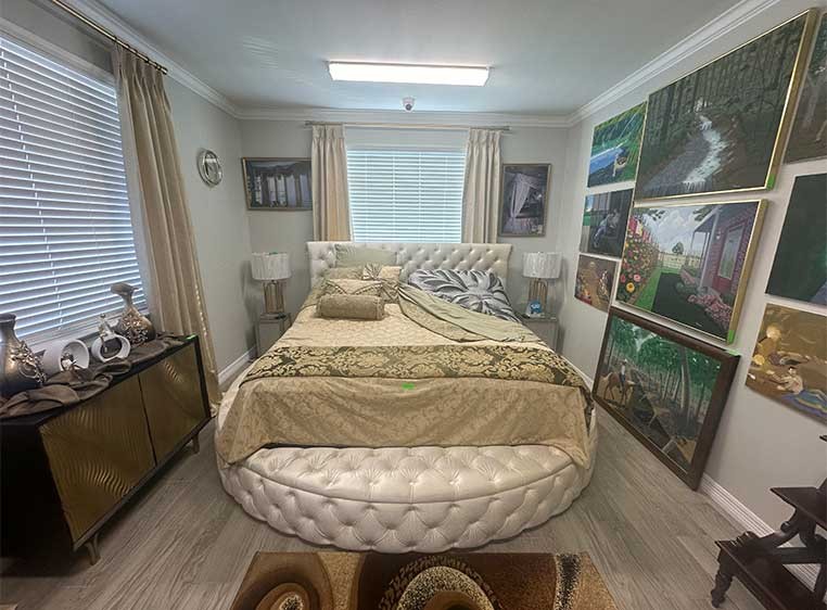 A bedroom featuring many pieces of art on the wall and two windows with Hunter Douglas blinds and drapery.